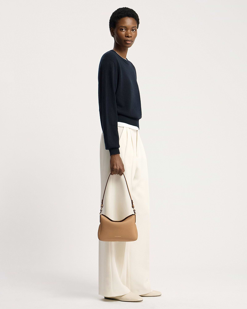 Model holding a caramel Strathberry Sway shoulder bag with top handle and visible logo.
