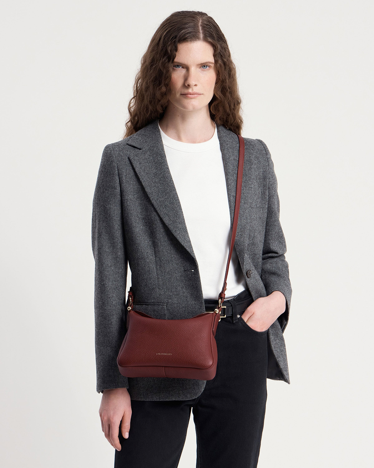 Model wearing a grey blazer and white t-shirt with oxblood Strathberry Sway bag.
