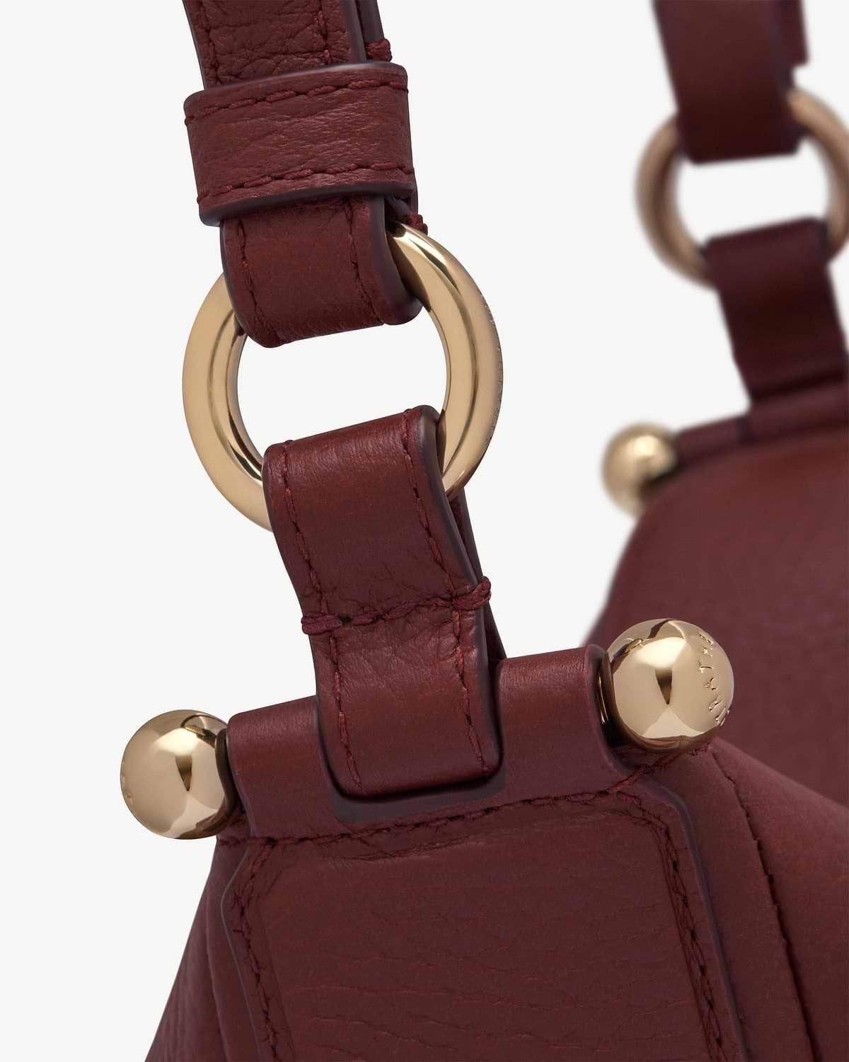 Oxblood leather strap with gold ring and stud hardware on a bag.