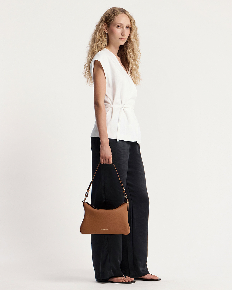 Model holding tan Sway Maxi shoulder bag with visible Strathberry wordmark.
