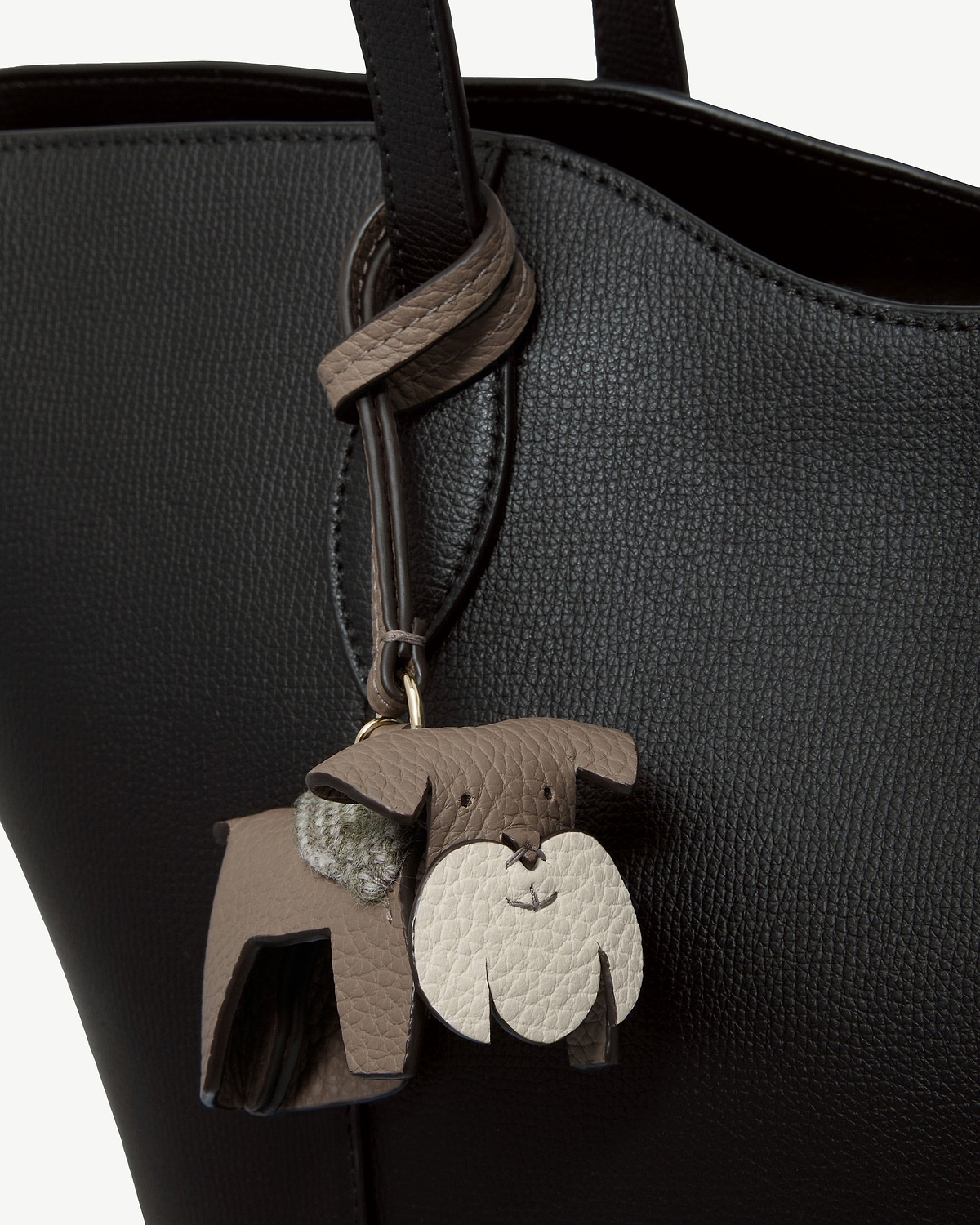 Taupe leather dog bag charm with cream face and tartan detail on black bag.