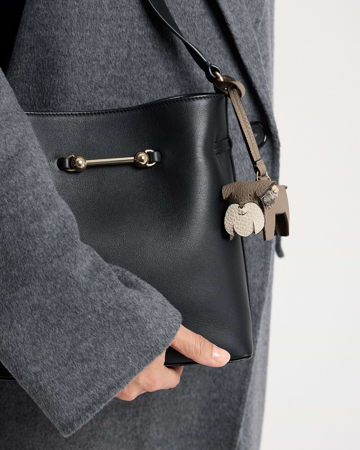 Beige tartan dog leather bag charm hanging from black leather bag and grey coat
