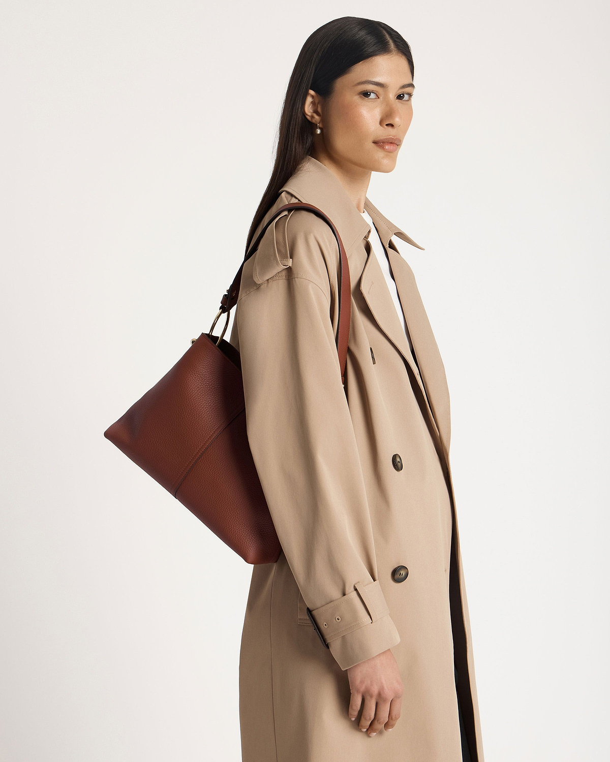 Model wearing beige trench coat carrying walnut brown leather hobo bag on shoulder