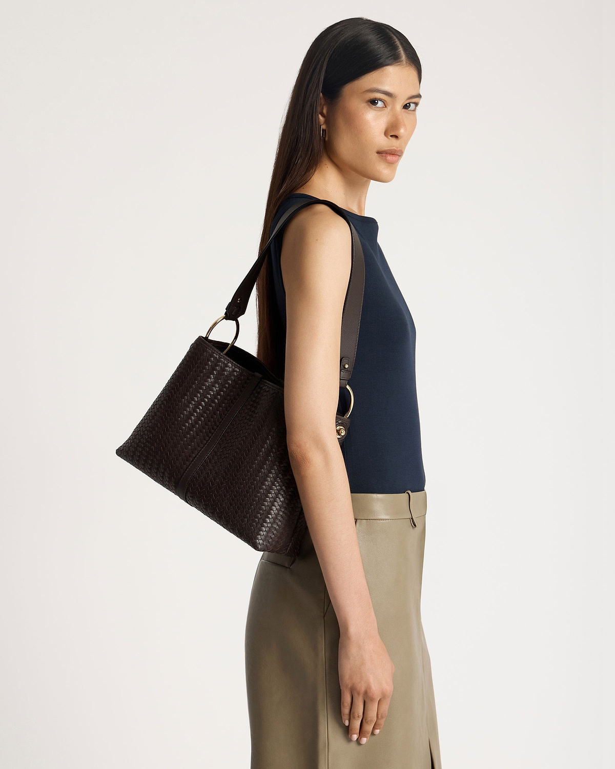 Woman wearing a navy sleeveless top carrying a chocolate woven leather hobo bag.