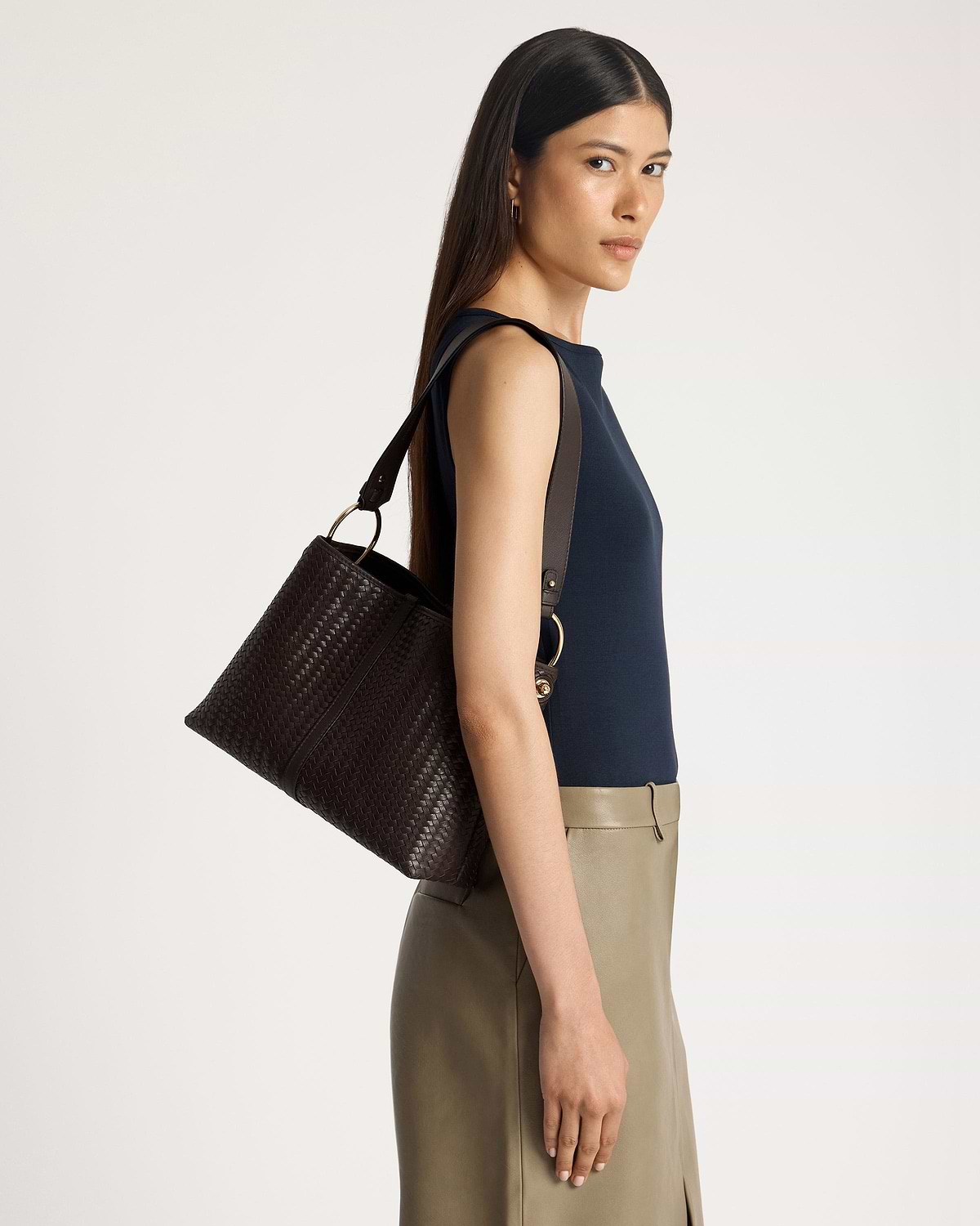 Woman wearing a navy sleeveless top carrying a chocolate woven leather hobo bag.