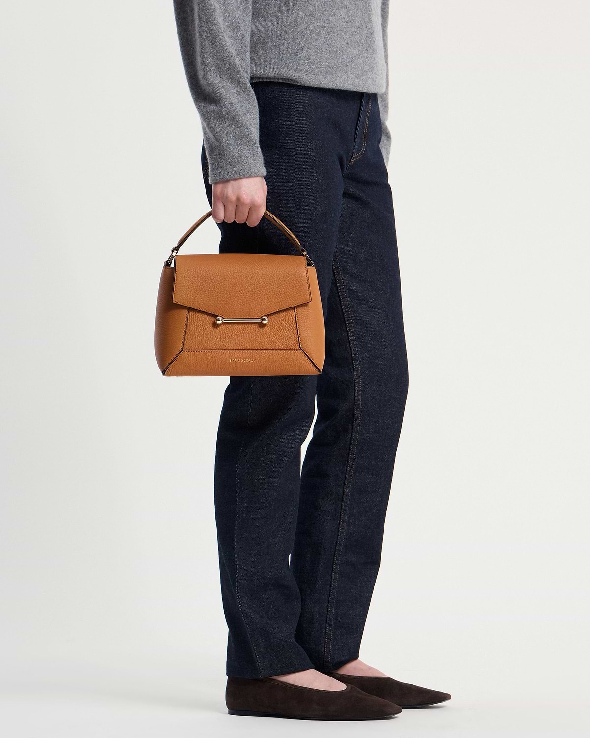 Model holds honey-coloured mosaic bag by top handle beside dark jeans.