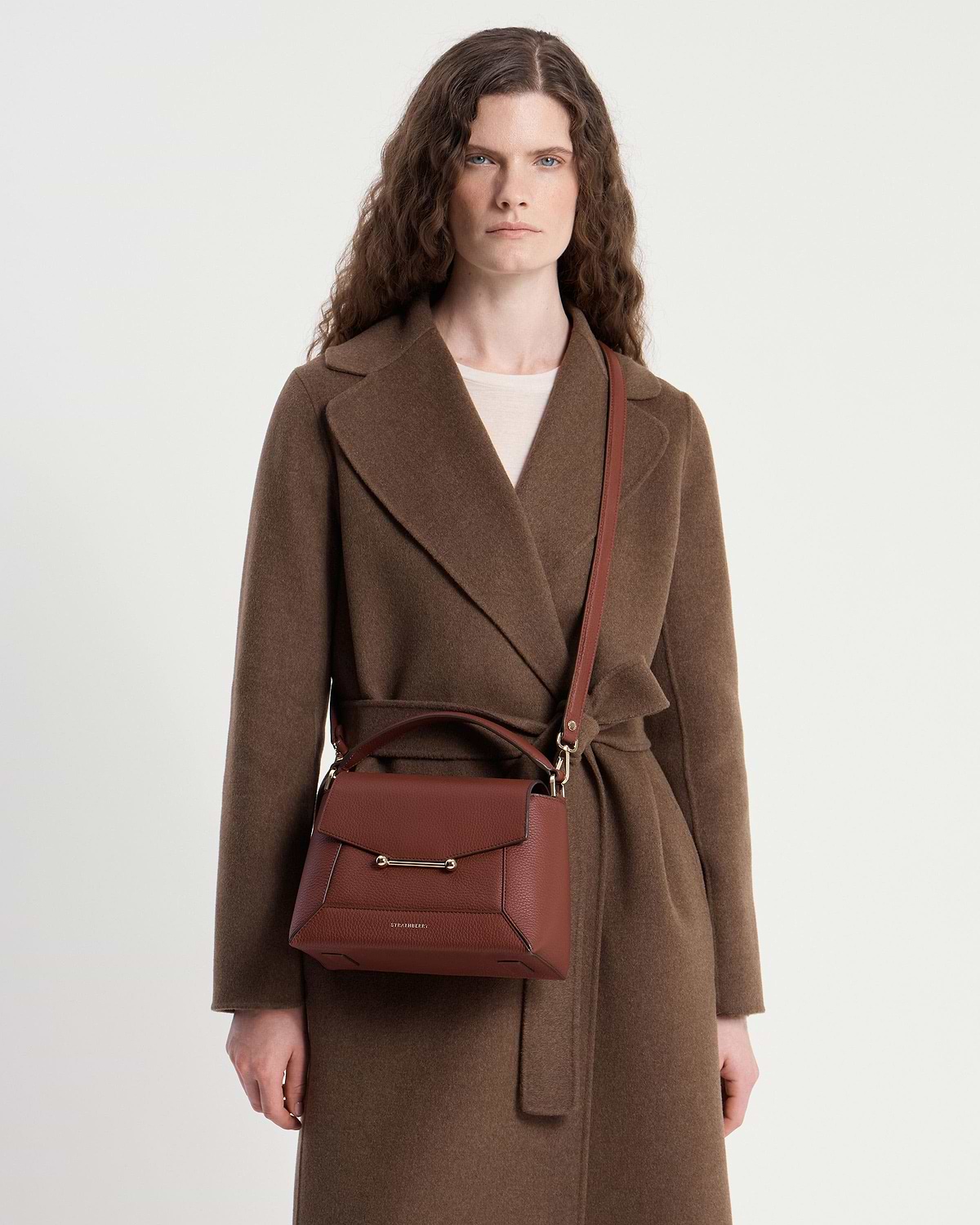 Model wearing brown coat with walnut mosaic crossbody bag, visible gold hardware.