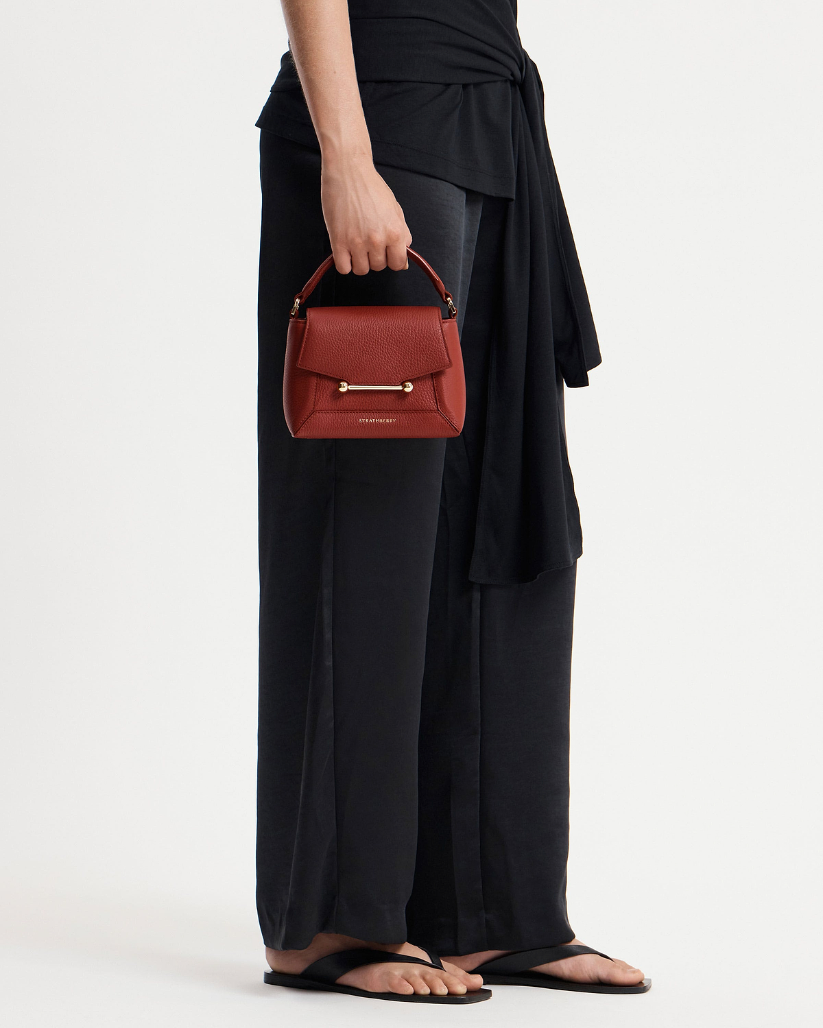 Model holding a Levanto red Strathberry Mosaic Nano handbag with gold bar.