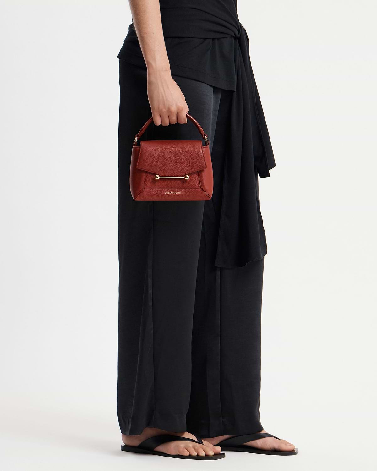 Model holding a Levanto red Strathberry Mosaic Nano handbag with gold bar.