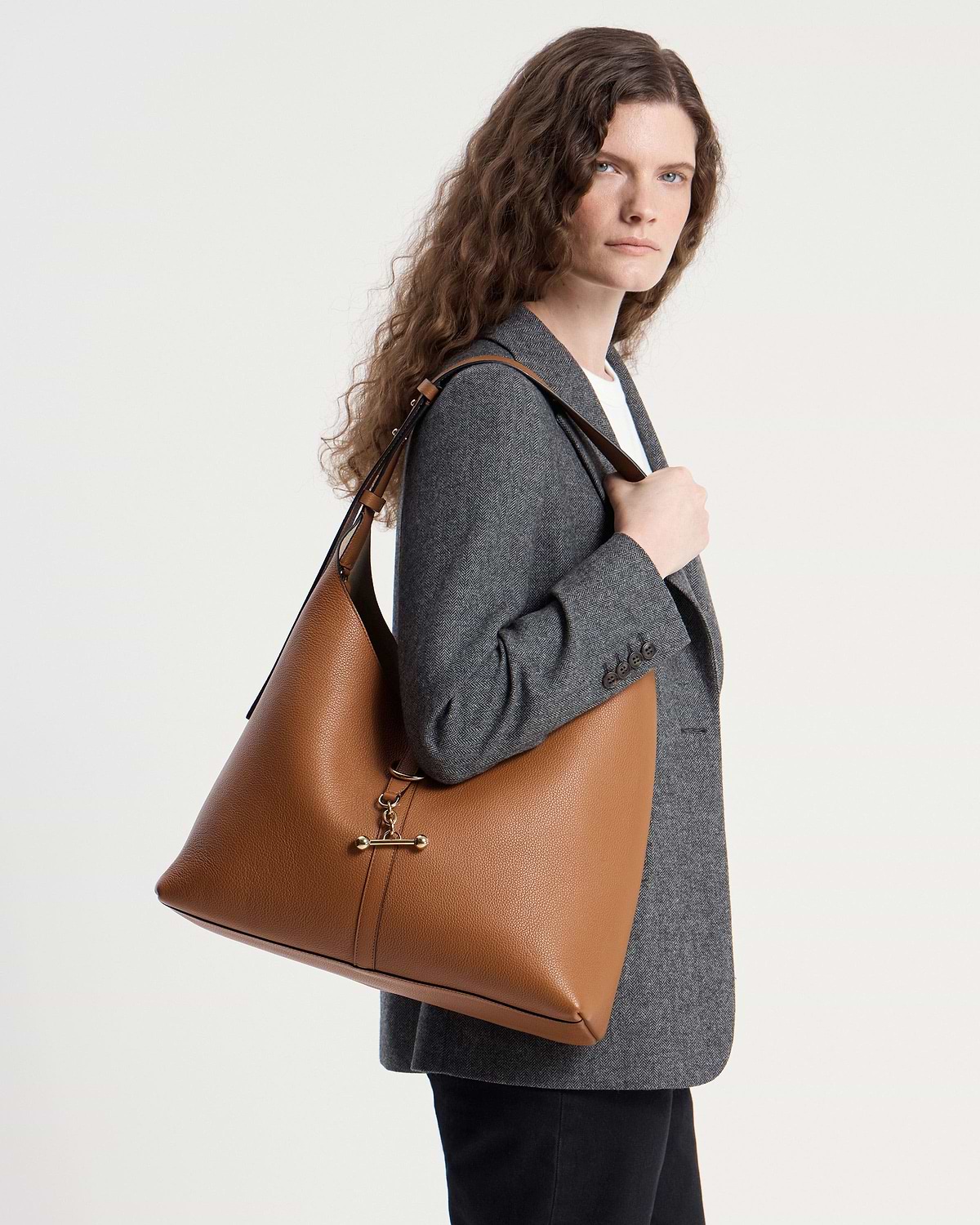 Woman wearing a tan leather hobo bag on her shoulder, grey blazer.