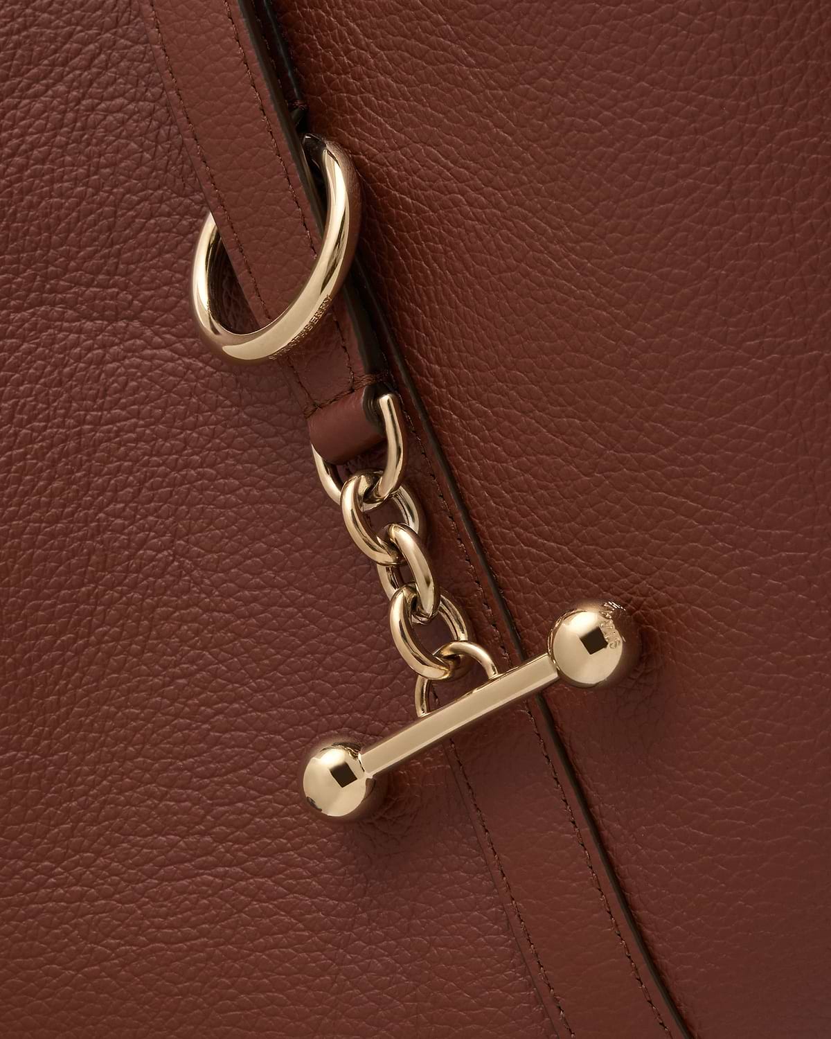 Close-up of walnut pebbled leather handbag strap with gold chain and toggle closure.