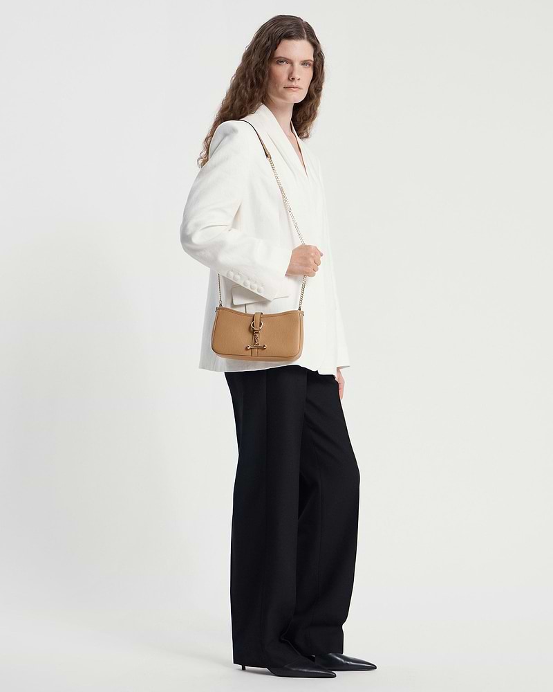 Caramel leather shoulder bag with gold chain strap worn by model in white blazer.