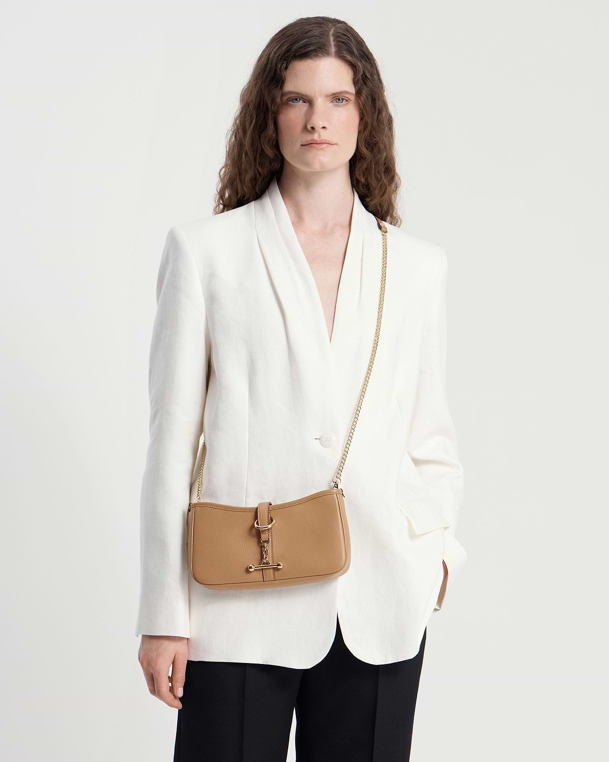 Model in a white blazer wearing a caramel leather Kite on a Chain bag