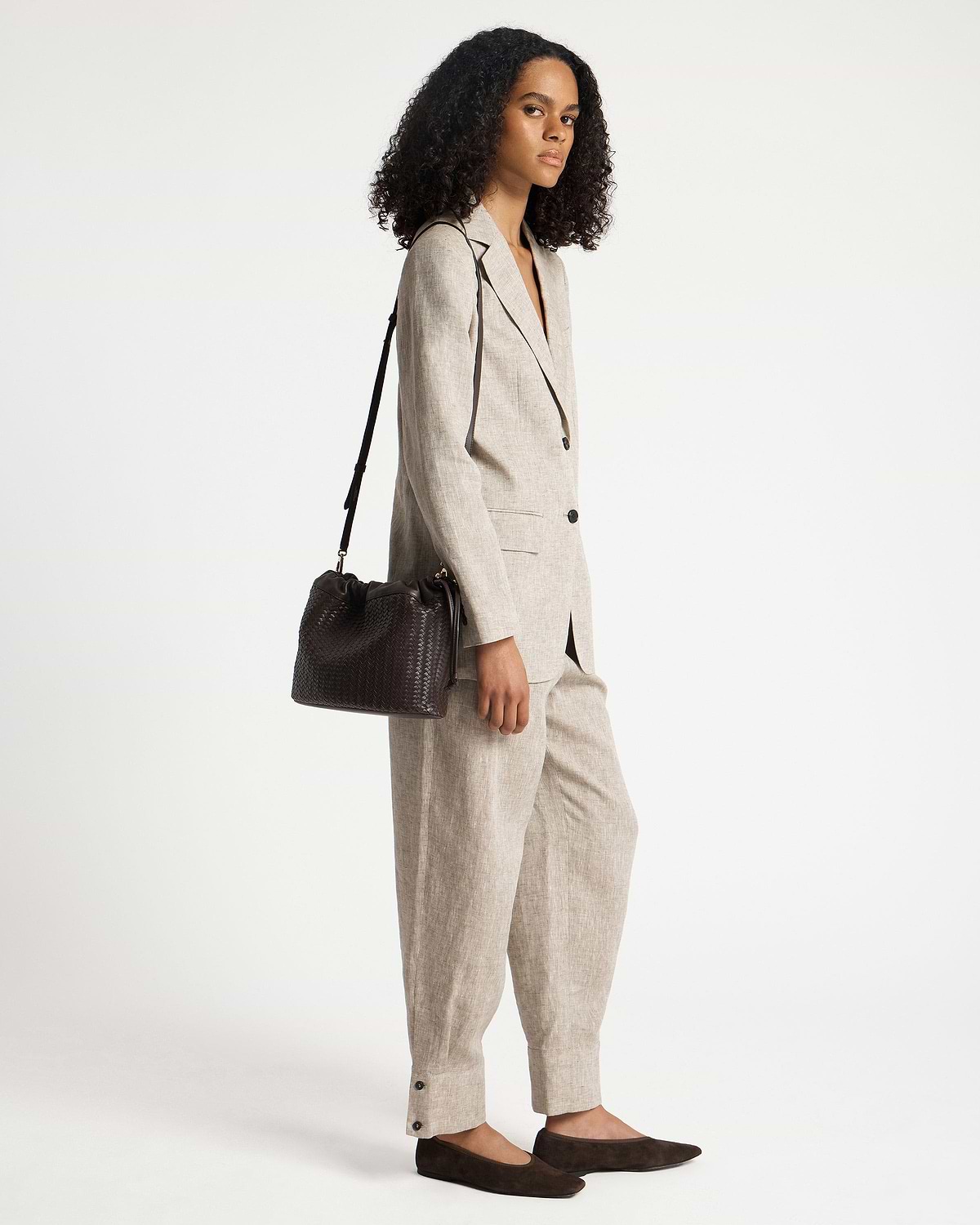 Model wearing a beige suit carrying a chocolate woven leather drawstring shoulder bag.