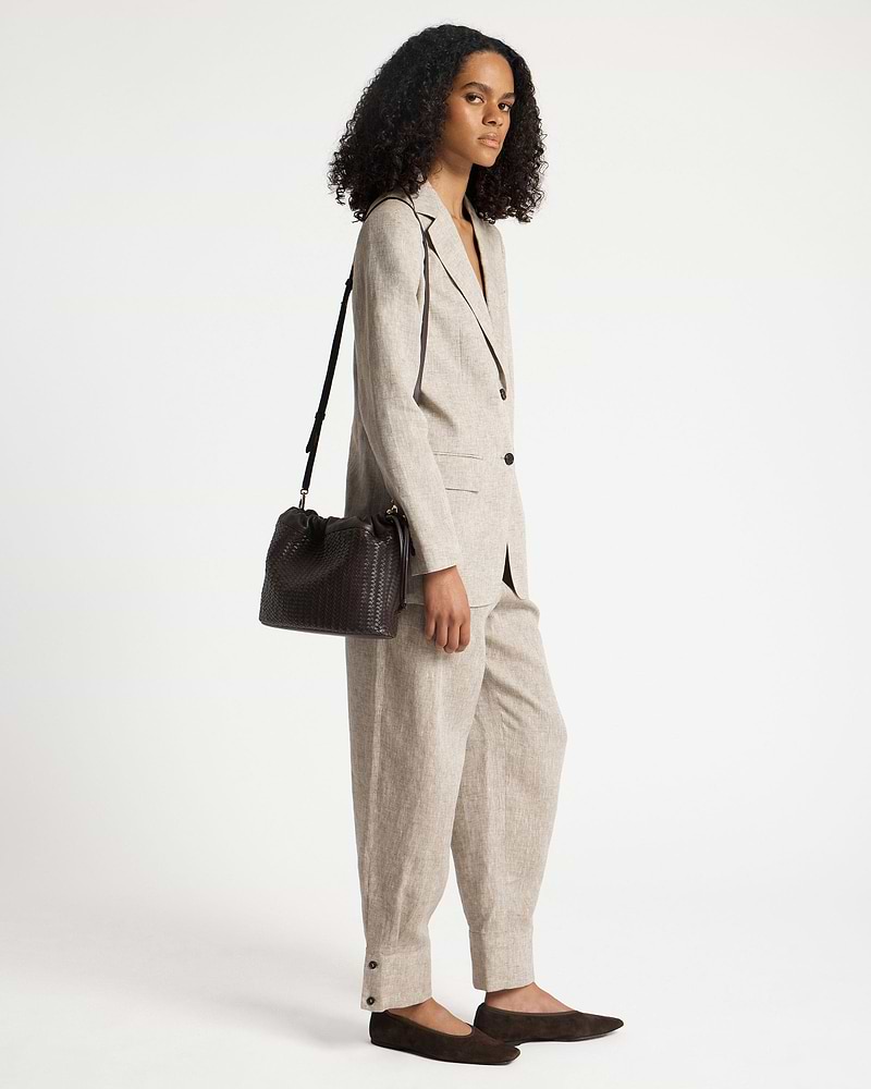 Model wearing a beige suit carrying a chocolate woven leather drawstring shoulder bag.
