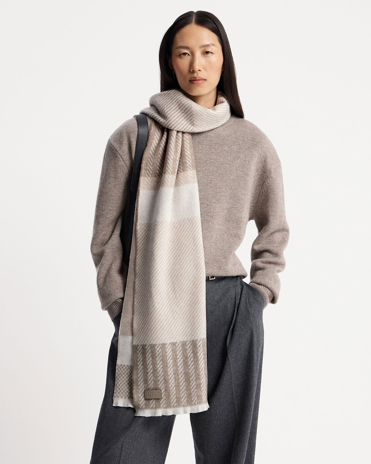 Model wearing taupe tartan cashmere scarf draped over shoulder, visible Strathberry logo.
