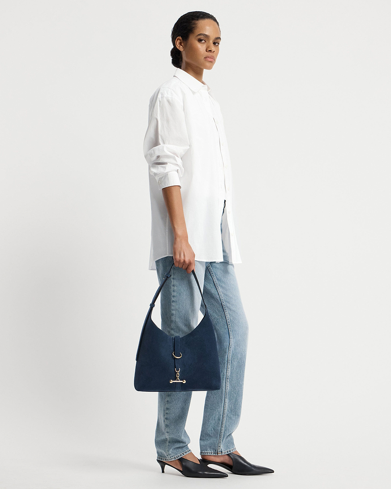 Model wearing a white shirt and jeans holding a loch blue suede Kite Hobo bag.