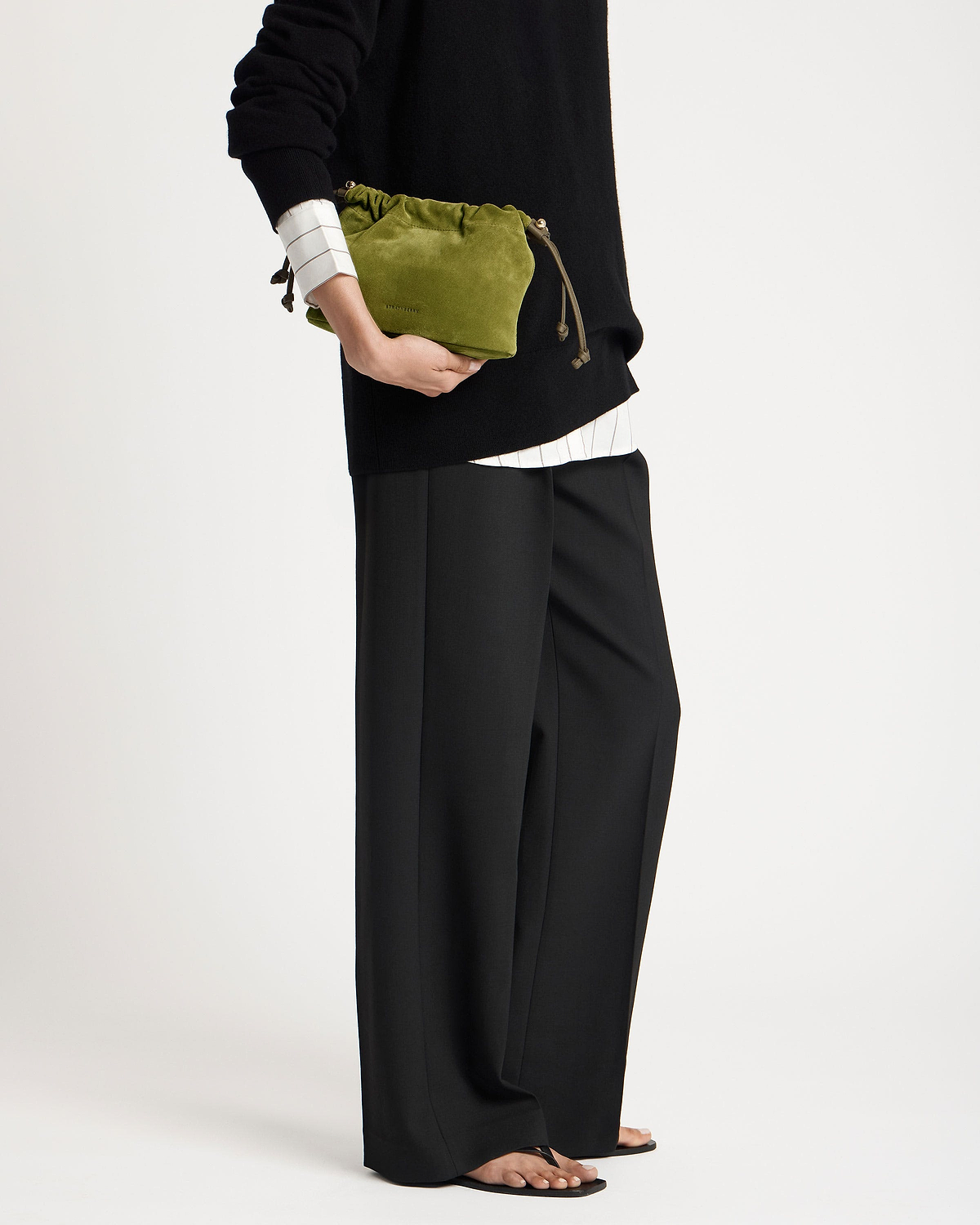 Lime suede drawstring bag with khaki cords held at model's hip.