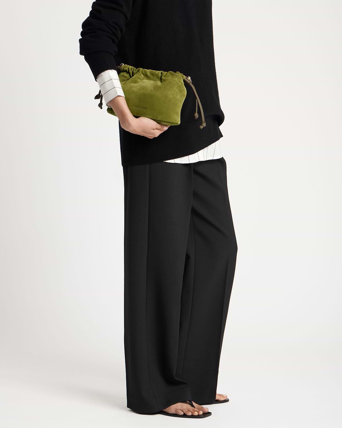 Lime suede drawstring bag with khaki cords held at model's hip.