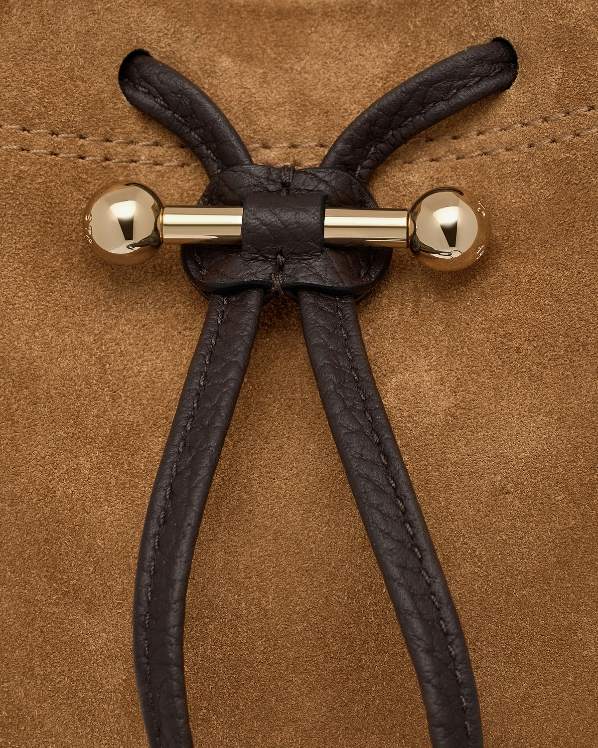 Gold bar toggle with espresso leather drawcord on toffee suede background.
