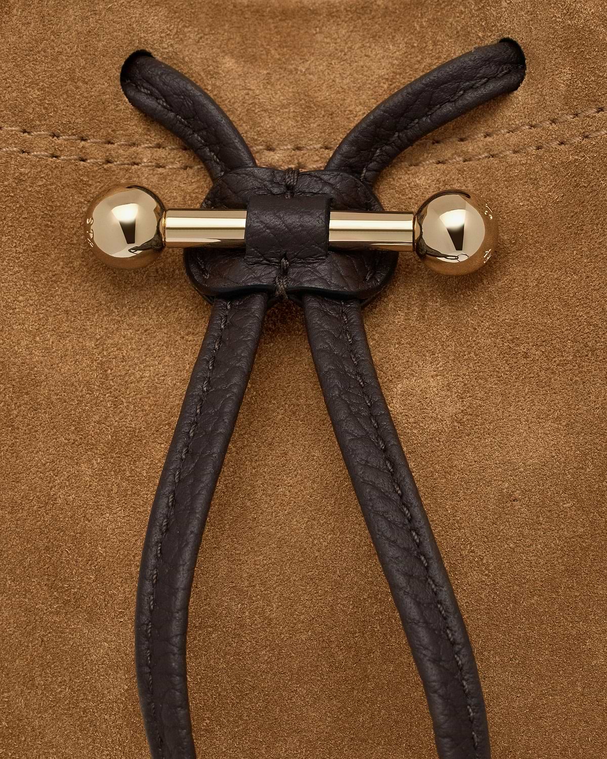 Gold bar toggle with espresso leather drawcord on toffee suede background.
