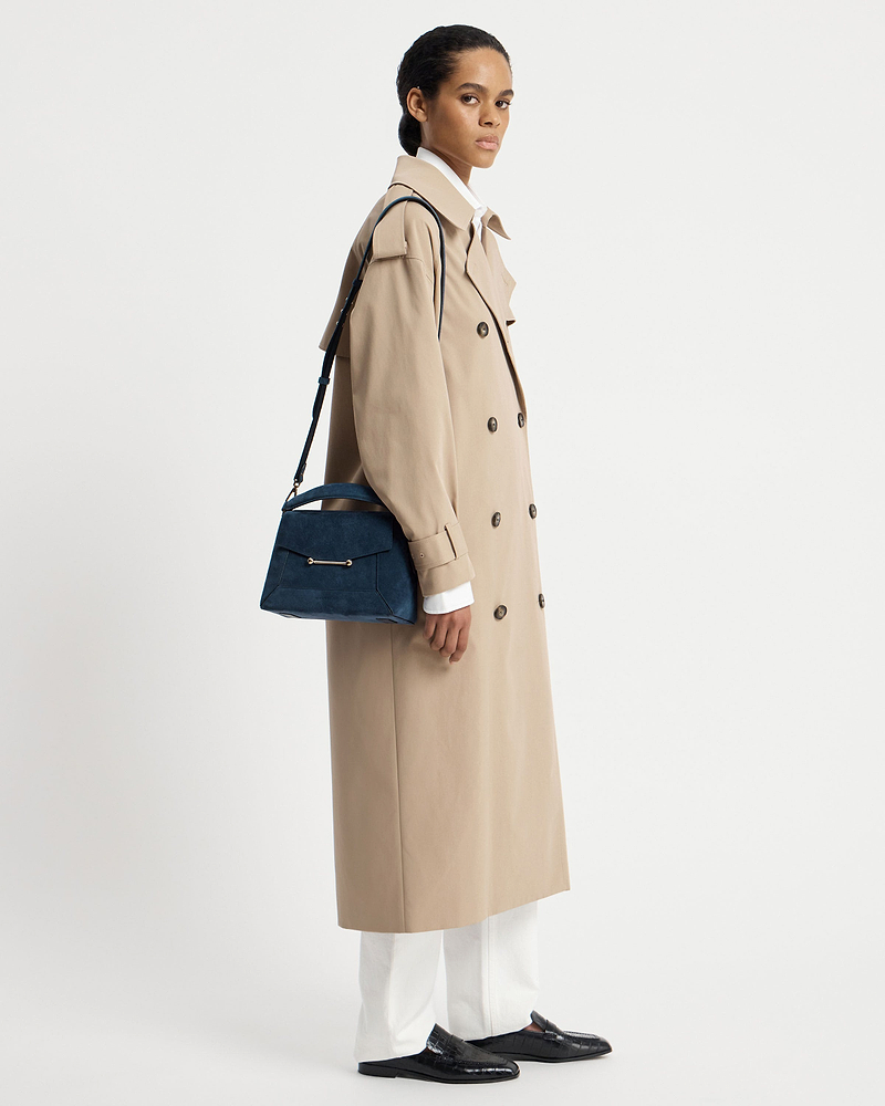 Model wearing beige trench coat carrying a loch blue suede mosaic bag.