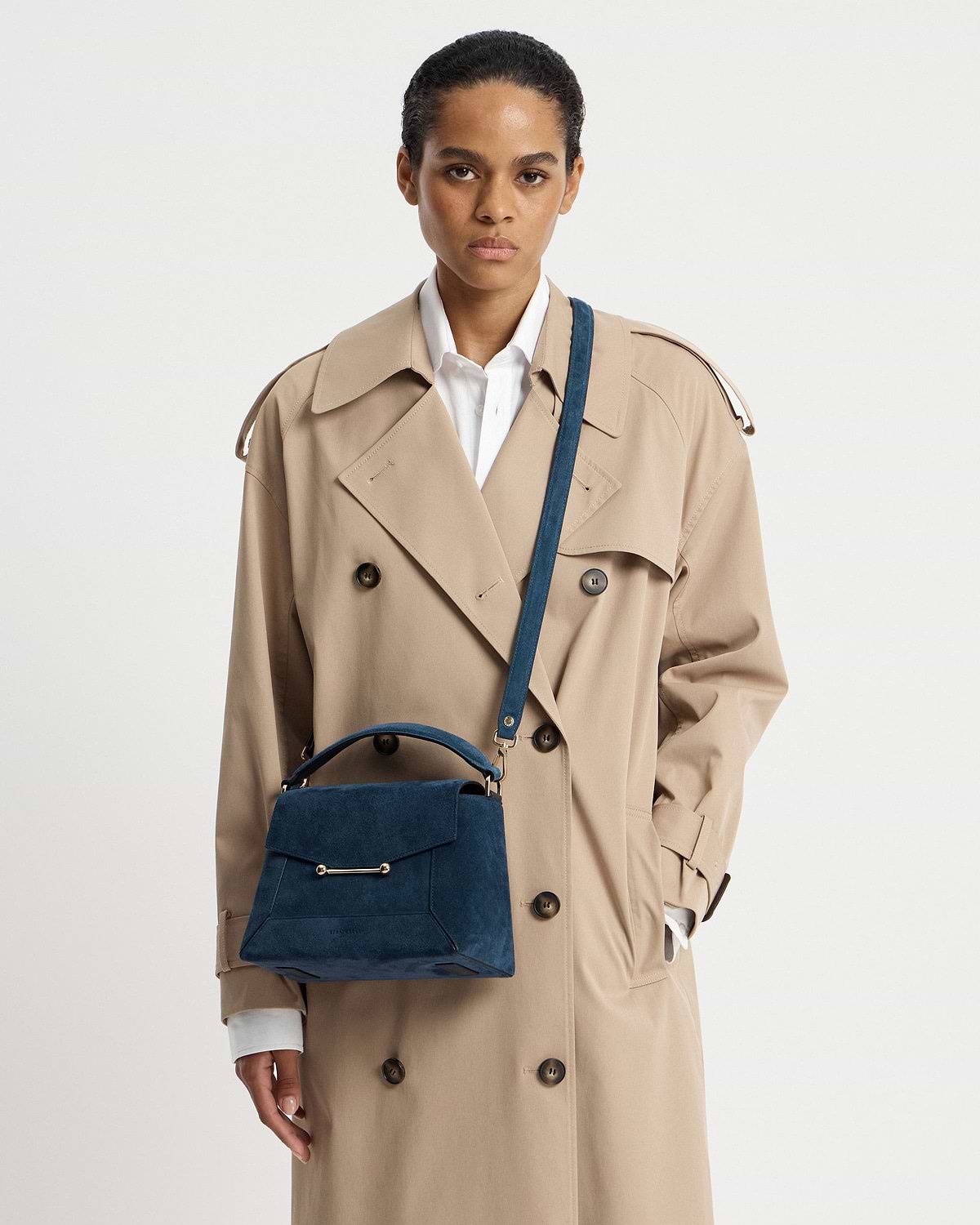 Model wearing beige trench coat with loch blue suede mosaic bag worn crossbody.