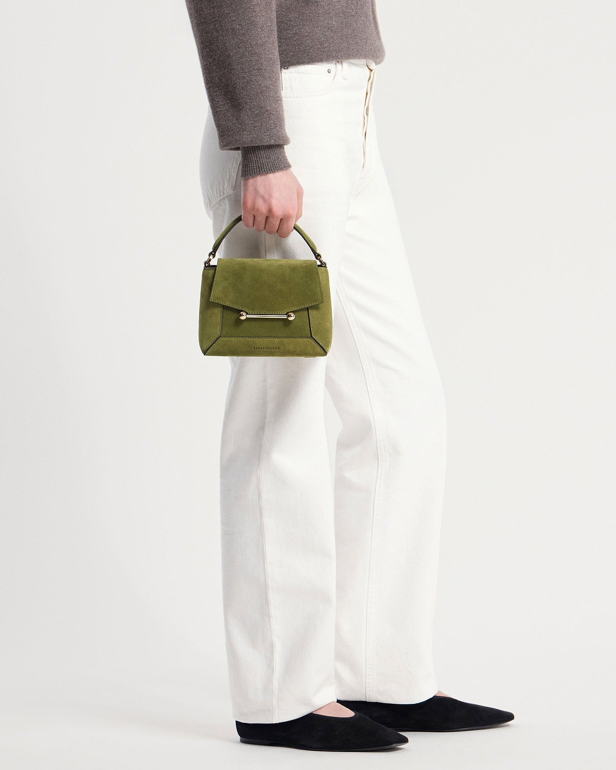 Strathberry Mosaic Nano lime suede mini bag held by model in white trousers.
