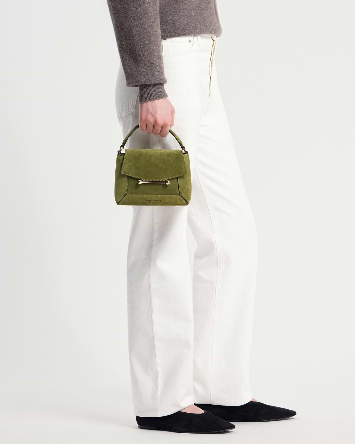 Strathberry Mosaic Nano lime suede mini bag held by model in white trousers.