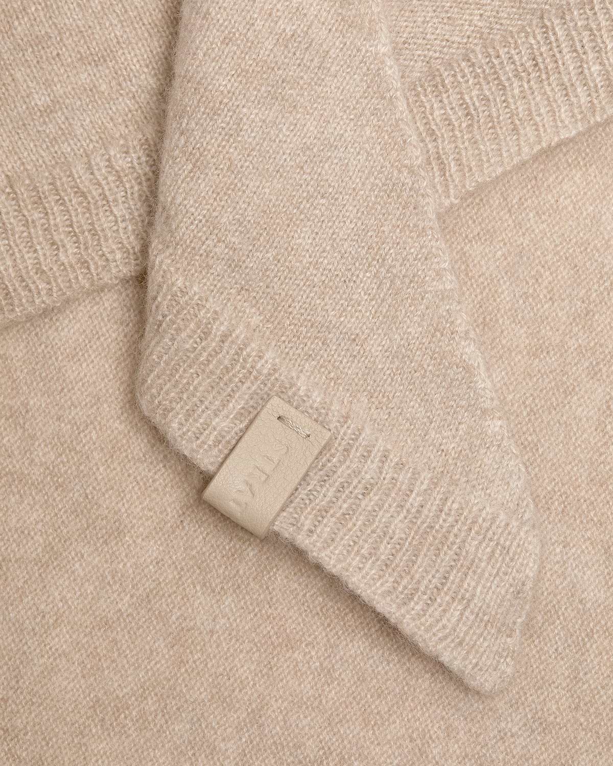 Oat-coloured cashmere bandana with visible knit texture and a small leather tag.