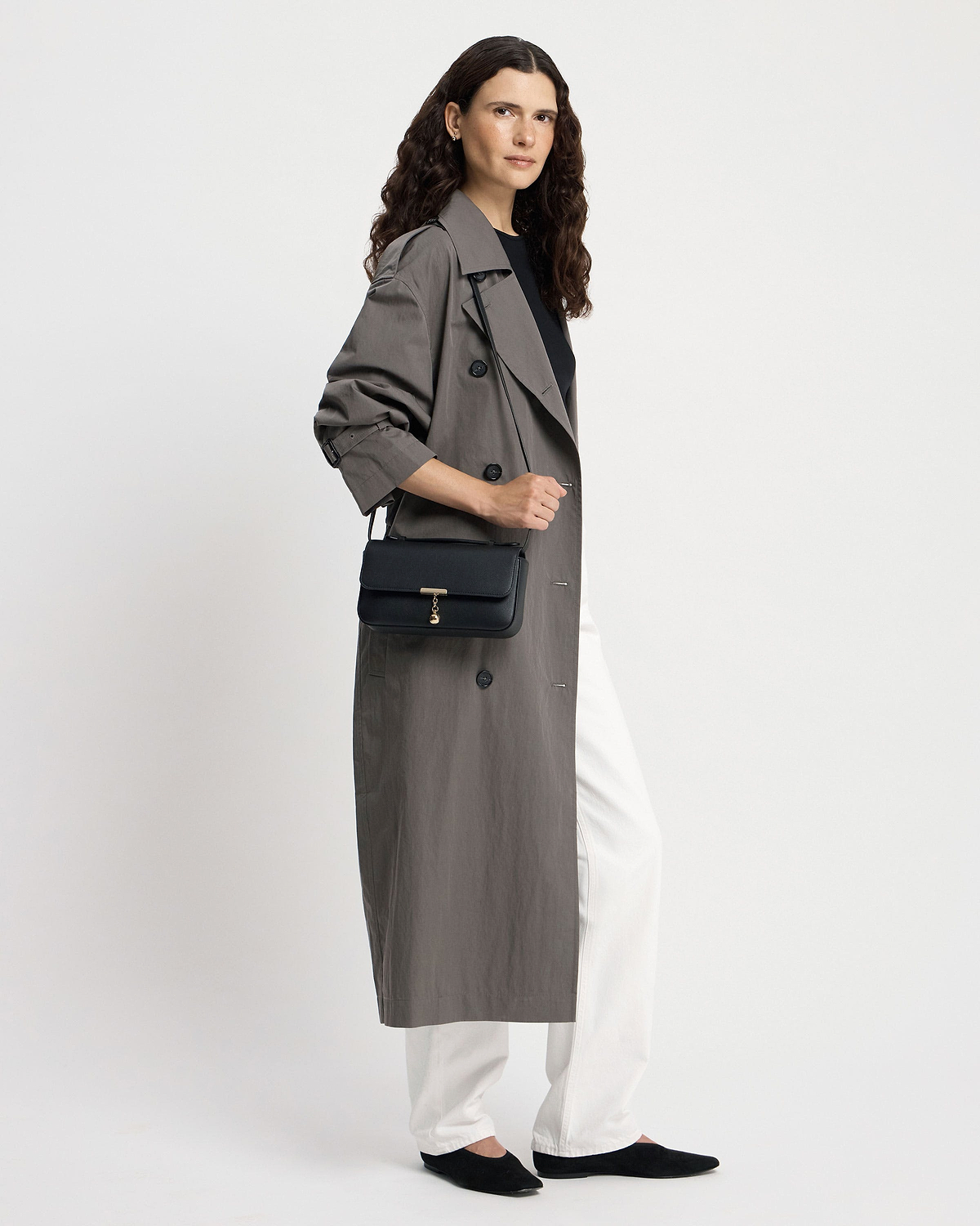 Woman wearing a trench coat carrying a black Nocturn clutch with gold clasp.