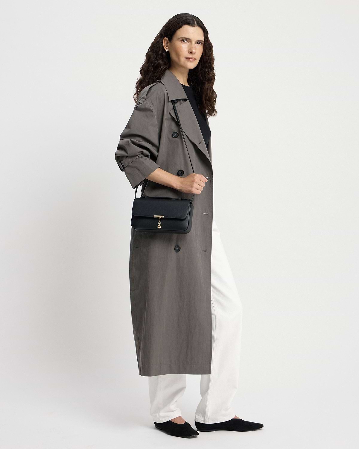 Woman wearing a trench coat carrying a black Nocturn clutch with gold clasp.