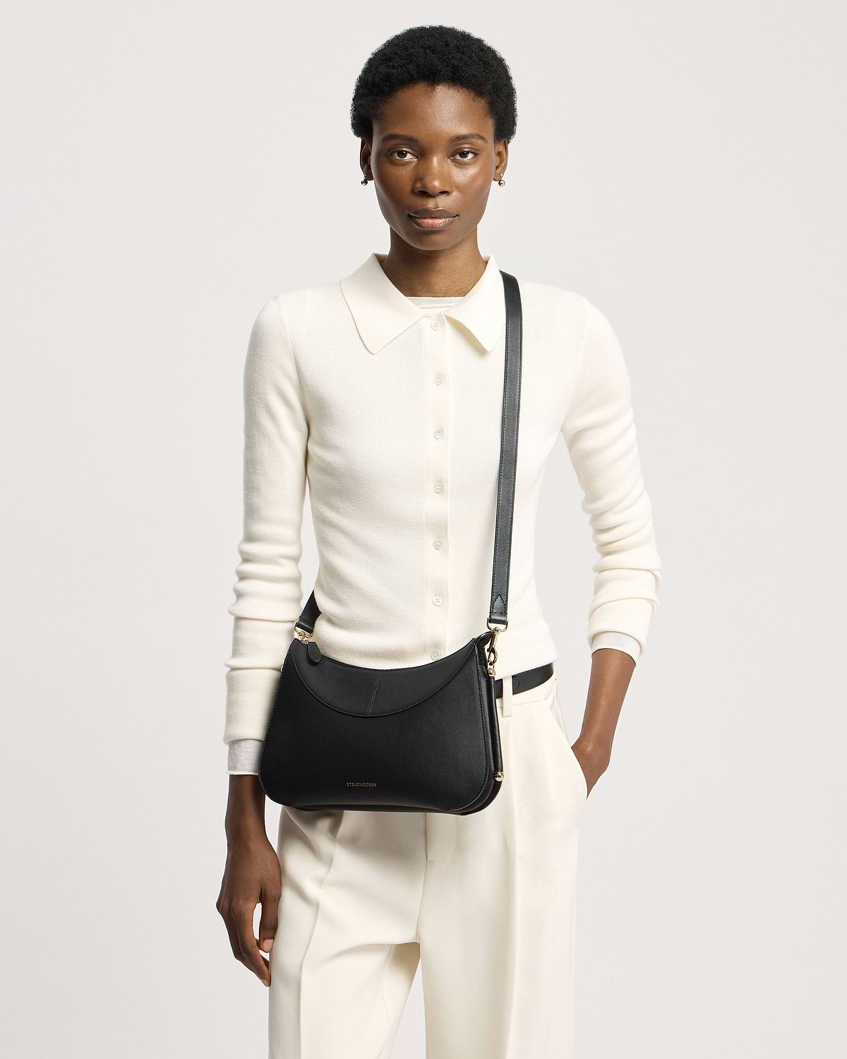 Model wearing cream top and trousers with black Strathberry Nest Shoulder bag.