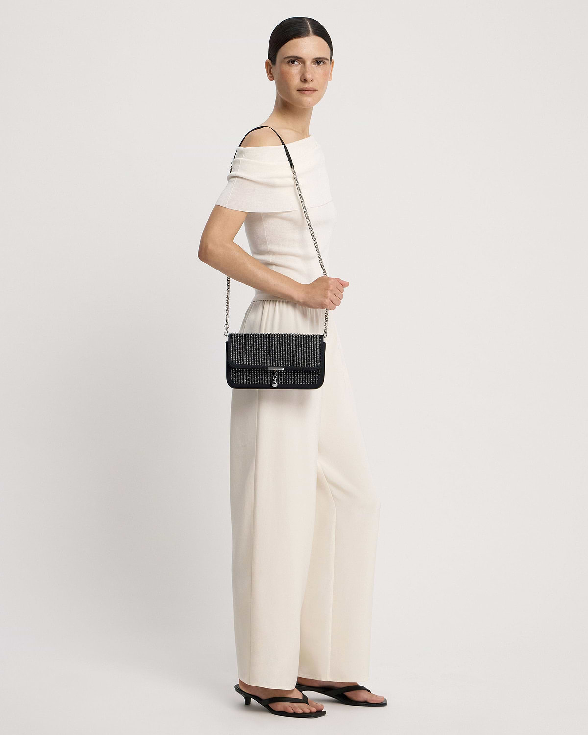 Model wearing a black embroidered satin clutch with a silver chain strap at hip.