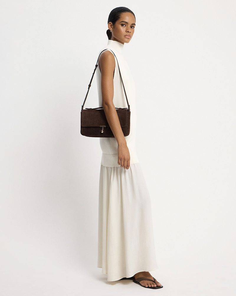 Model in white dress carrying espresso suede Nocturn Midi shoulder bag
