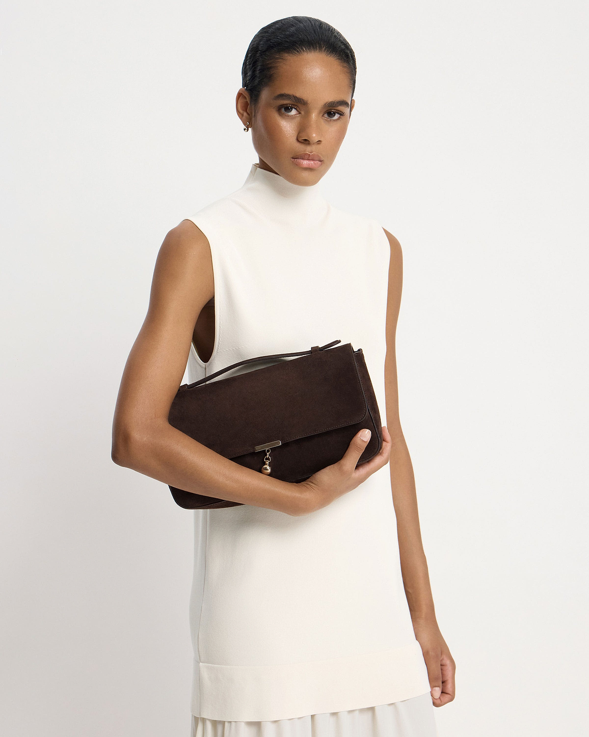 Model in white sleeveless dress holding espresso suede Nocturn Midi shoulder bag.