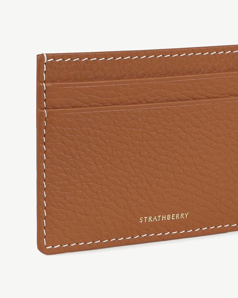 Tan leather cardholder corner with vanilla contrast stitching and gold Strathberry logo.