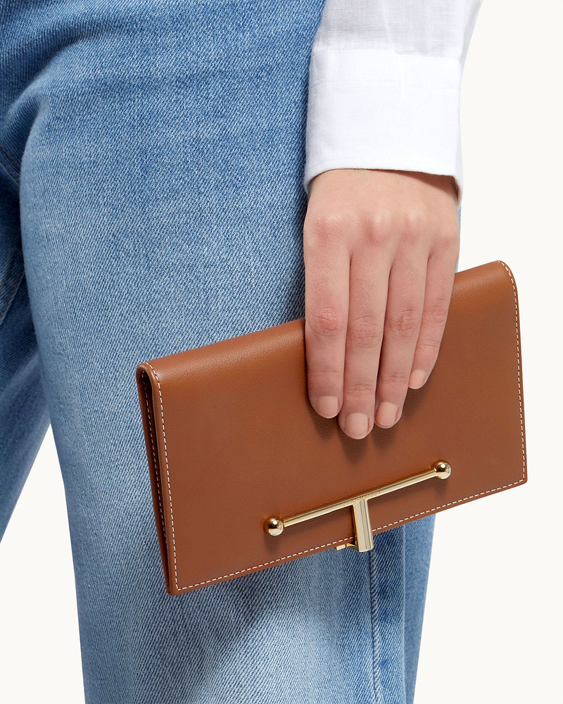 Hand holding chestnut large Melville Street wallet with vanilla stitching and gold bar.