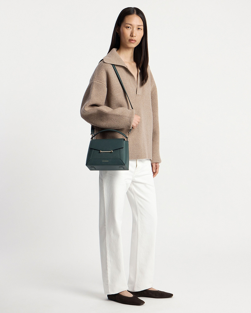 Model wearing beige jumper and white trousers holding bottle green mosaic bag.