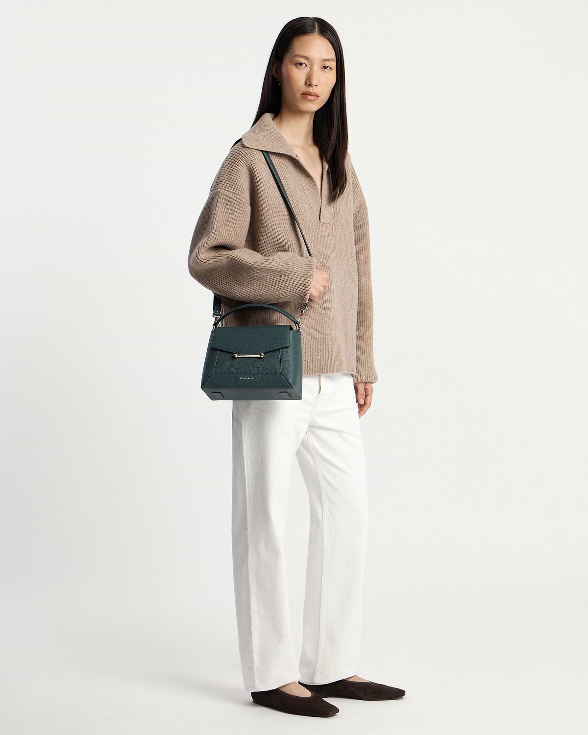 Model wearing beige jumper and white trousers holding bottle green mosaic bag.
