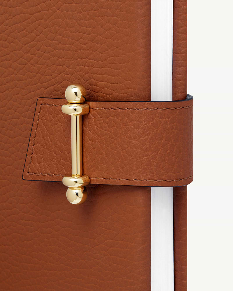 Tan leather notebook cover with gold bar closure and visible white page edges.