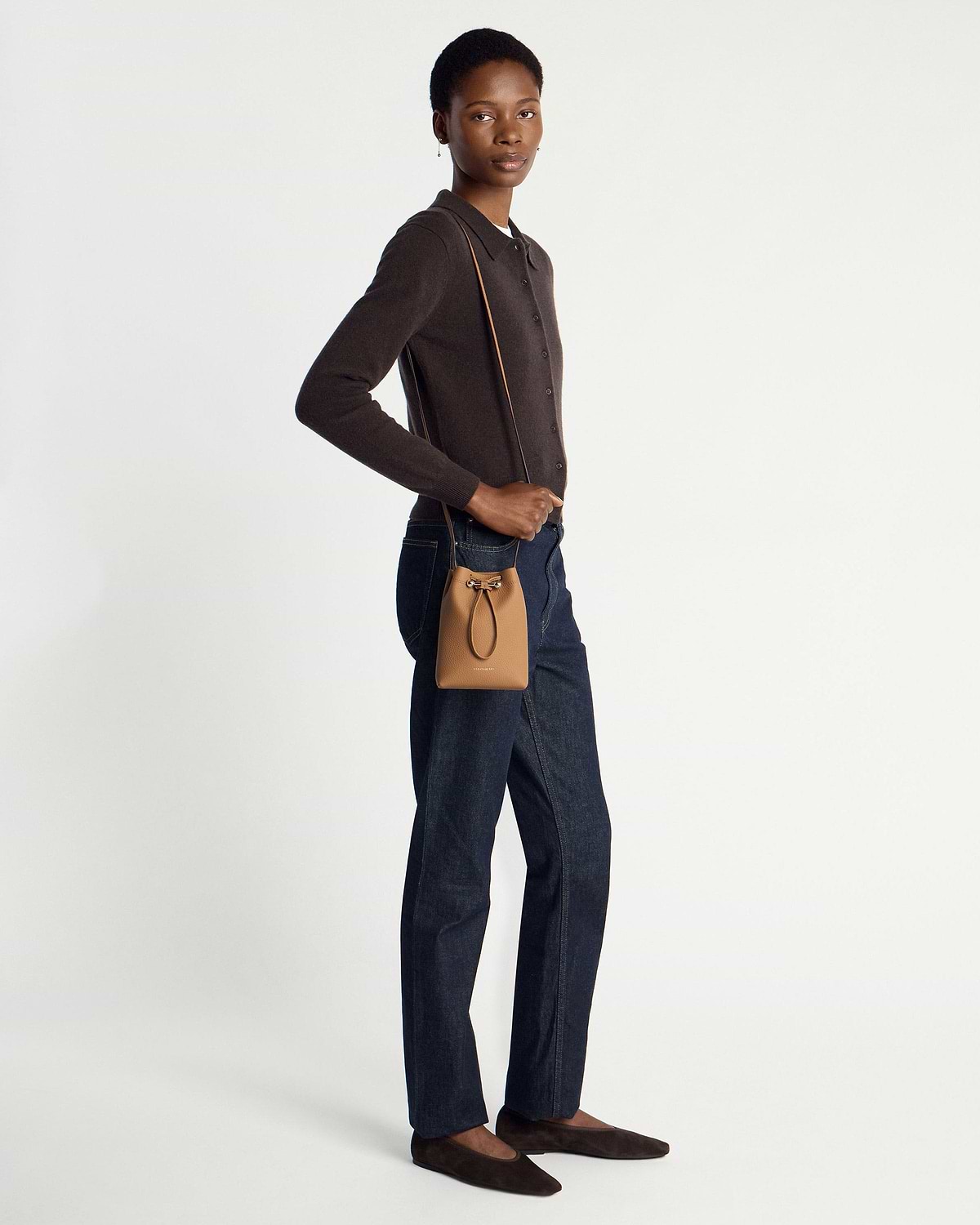 Model wearing caramel midi pouch crossbody with dark cardigan, jeans, brown flats.