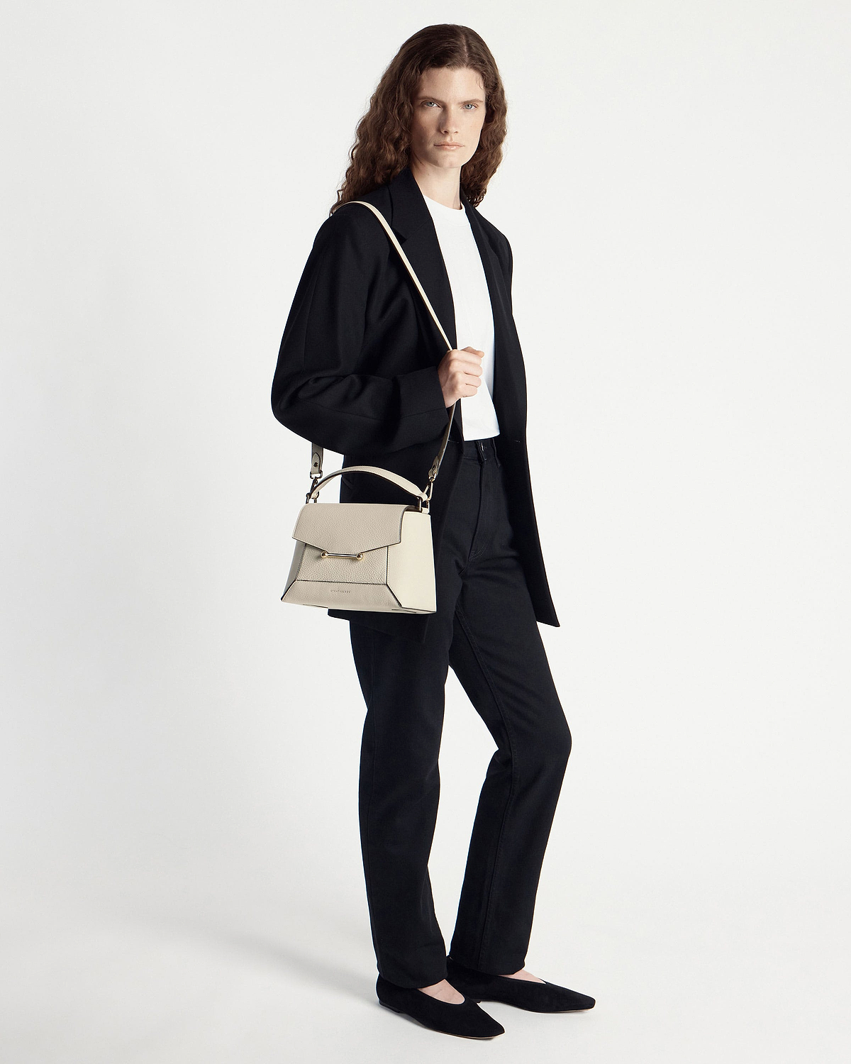 Model in black outfit holding vanilla mosaic bag with top handle and shoulder strap.