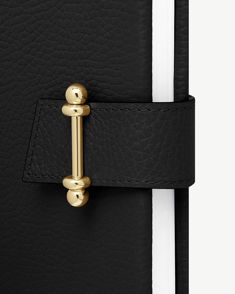 Black leather notebook with gold bar clasp and white page edges.