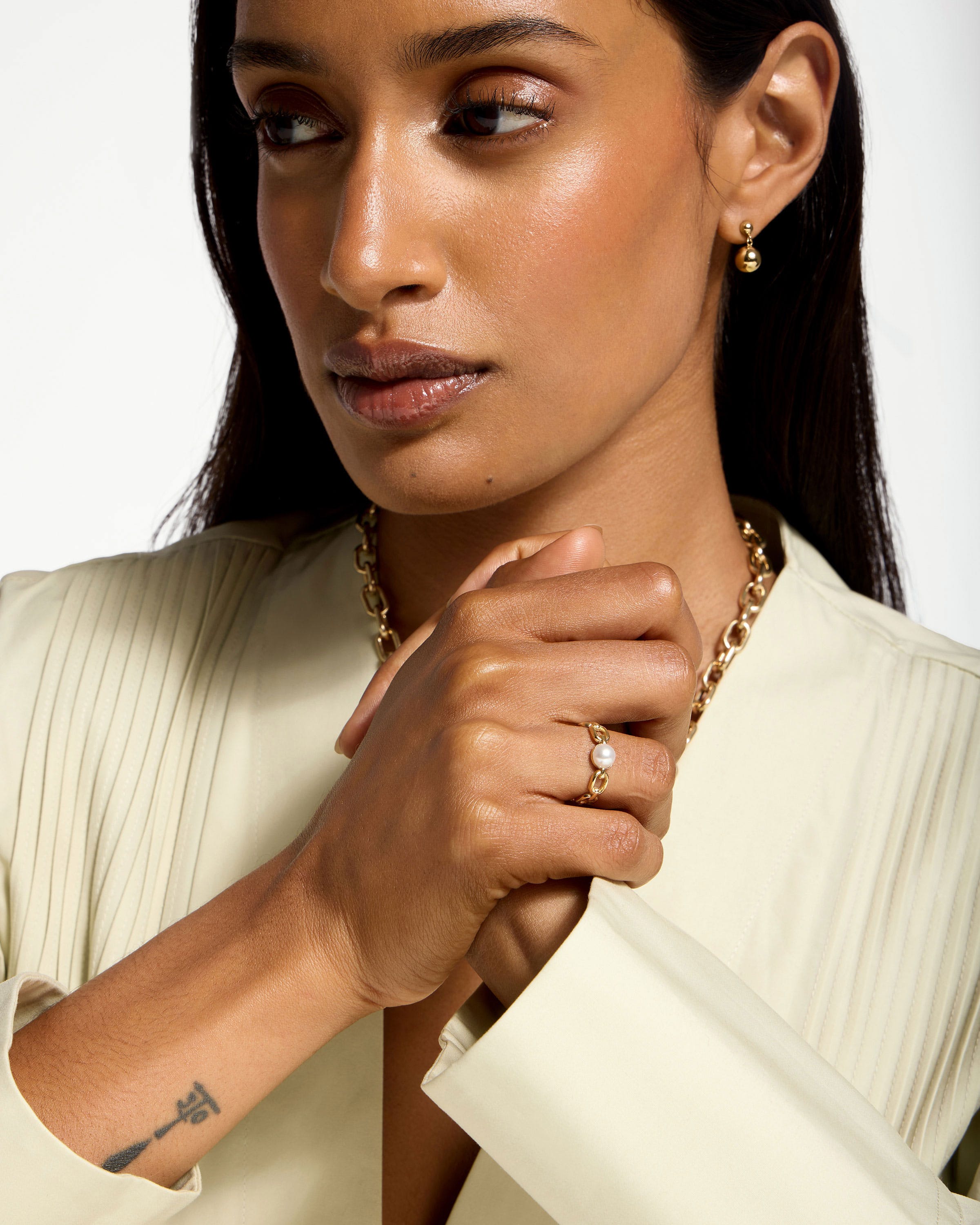 Woman wearing 22 carat gold gilded pearl link ring on clasped hands.