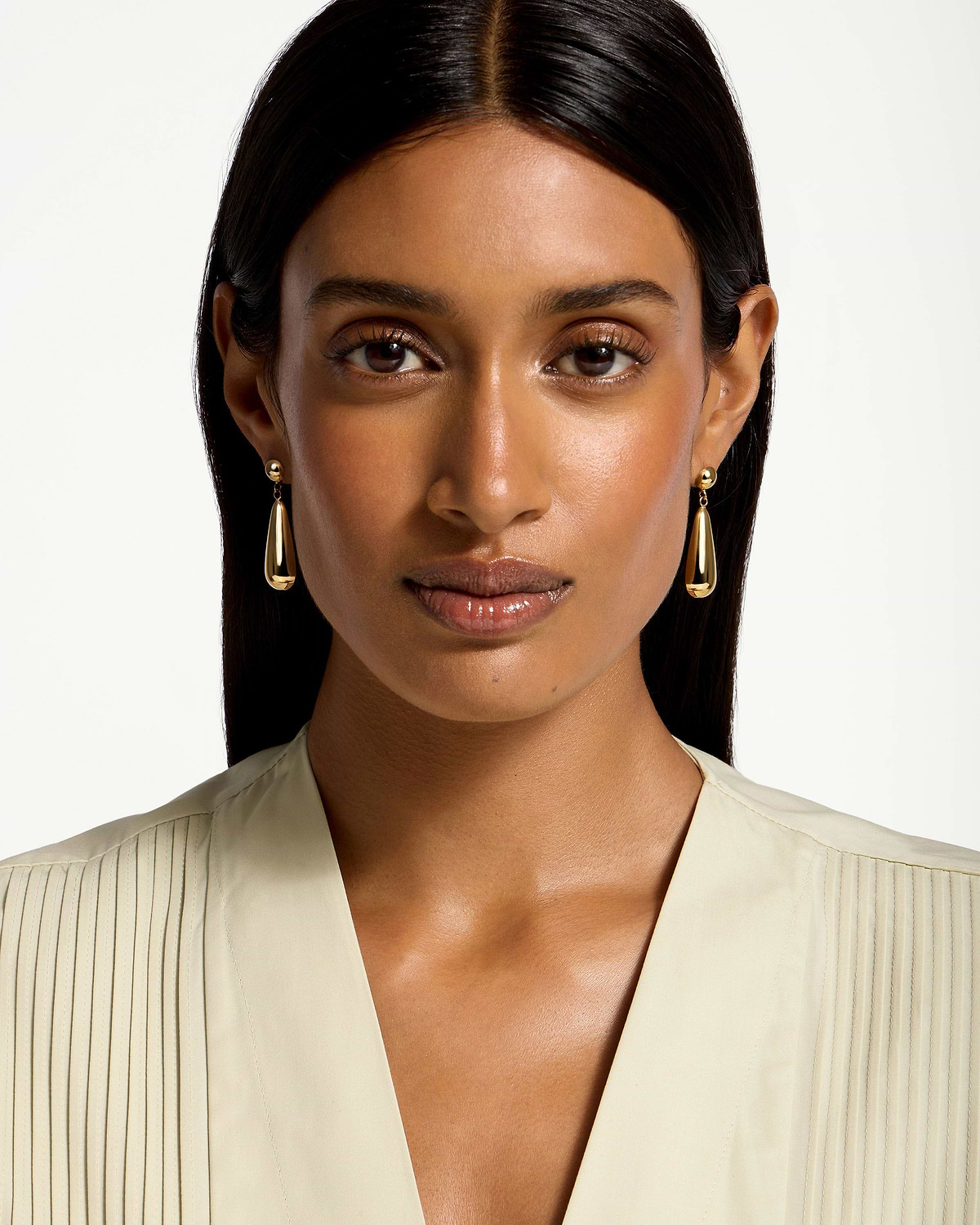 Woman wearing 24 carat gold gilded teardrop earrings, head and shoulders visible.