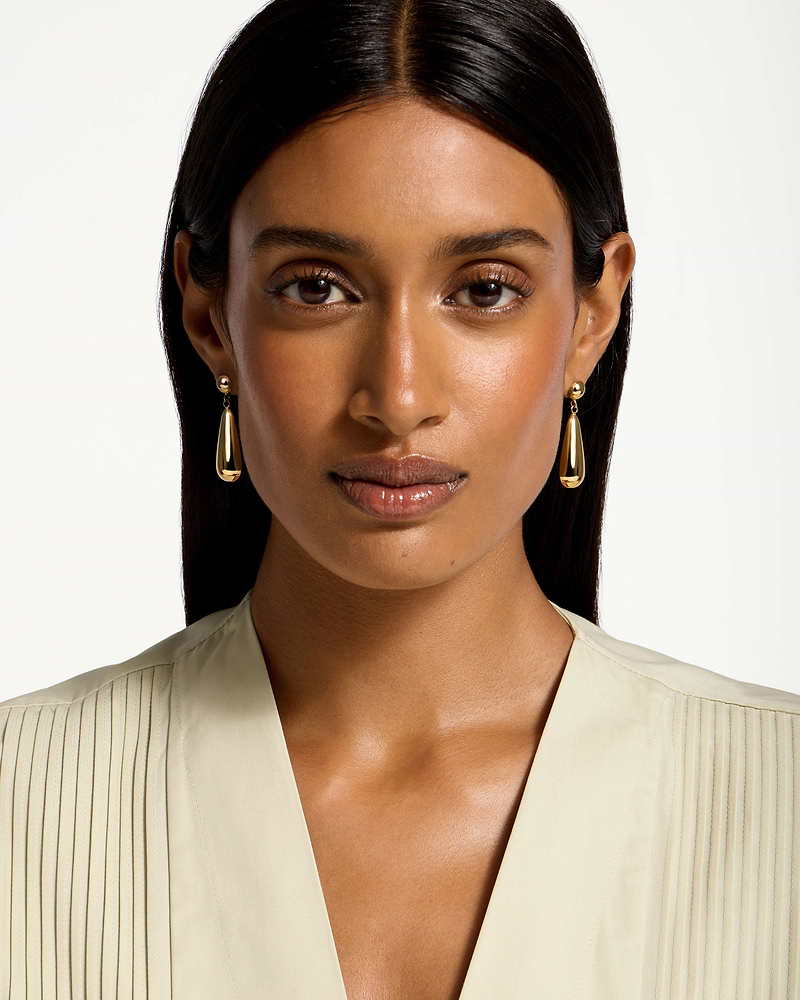 Woman wearing 24 carat gold gilded teardrop earrings, head and shoulders visible.
