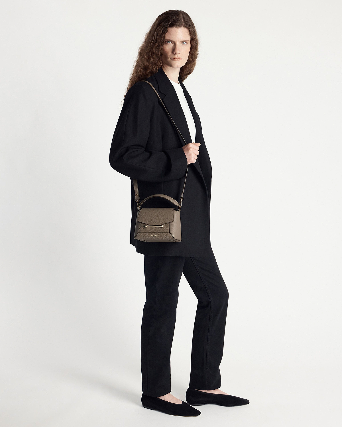 Model wearing a taupe small top-handle crossbody bag over the shoulder.