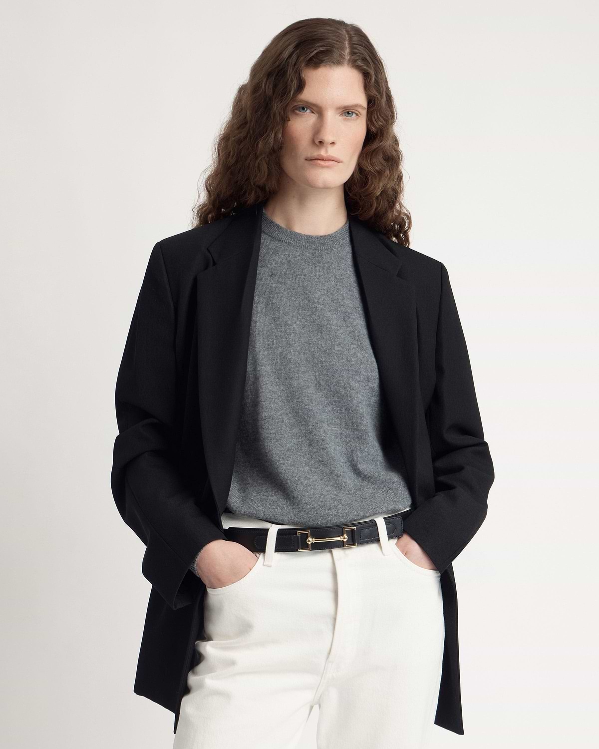Model wearing black leather belt with gold hardware over white trousers and grey sweater.