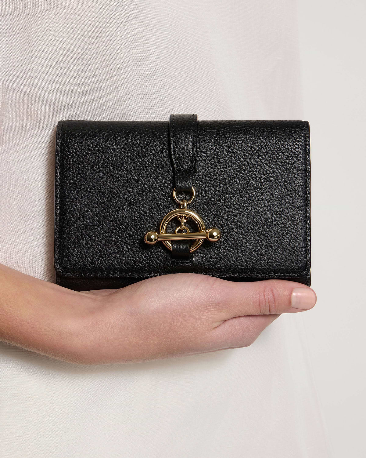 Black leather trifold wallet with gold turn-lock, held in one hand.